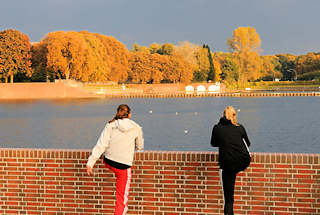 1366 Zwei Joggerinnen machen Lockerungsbungen an der Kaskade vom Stadtparksee im Stadtpark von Hamburg Winterhude - am gegenber liegenden Seeufer hohe Bume in Herbstfrbung.