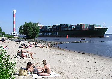 011_25831 | Badegste sonnen sich im Sand an der Elbe; ein Containerschiff verlsst hoch beladen Hamburg und fhrt Richtung Nordsee.