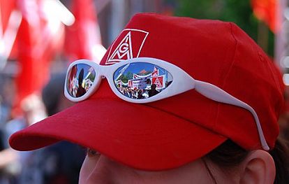 011_25931 |  eine rote Mtze mit dem IGM Aufdruck, dem Logo der IG Metall; in der Sonnenbrille spiegeln sich Transparente und Teilnehmer der Maikundgebung / Maidemonstration zum 1. Mai - Tag der Arbeit.  