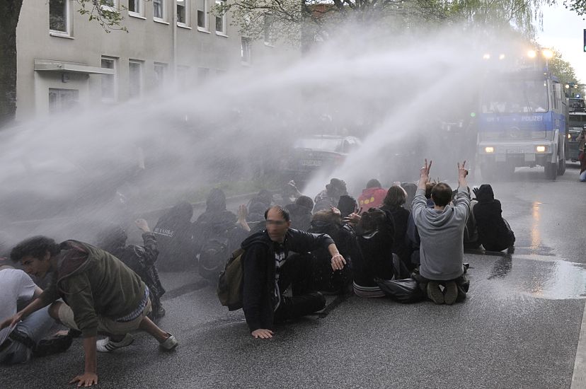 011_26020 |  Der Wasserwerfer versucht die Strassenblockierer aus zwei Rohren mit einem Wasserstrahl von der Strasse zu treiben. Zunchst halten die Demonstranten dem hohen Druck der Wasserkanone stand.