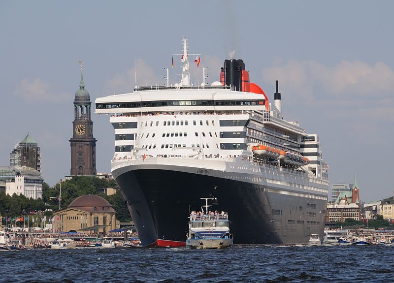 96-4382 |Die Queen Mary 2 verlsst den Hafen der Hansestadt Hamburg. Im Hintergrund der hohe Kirchturm des Hamburger Wahrzeichens, die St. Michaeliskirche. Die R.M.S.(Royal Mail Ship)  Queen Mary 2 (QM2) ist mit 148.528 BRZ eines der grten Passagierschiff der Welt. Das britische Kreuzfahrtschiff  hat eine Lnge von 345 m und eine Breite von 45 m. Der Luxuslinerbietet in 1310 Kabinenbis zu 2.620 Passagieren Platz und hat eine Besatzung von 1.253 Personen. Die Queen Mary 2 hat fnf Swimmingpools, einen Ballsaal, Golfanlage, Wintergarten, Sportzentrum, mit ber 8.000 Bchern die grte Bibliothek auf See, den grten ffentlichen Saal (Restaurant Britannia), der ber zwei Decks und die gesamte Schiffsbreite geht, acht weitere Restaurants, Fitness-Center, Planetarium, Kino, Theater. www.fotograf- hamburg.de