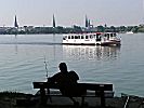 011_25828 | Hamburg Panorama mit den Kirchtrmen der Hauptkirchen; der Alsterdampfer fhrt auf der Aussenalster Richtung Winterhude - ein Angler sitzt auf einer Bank und beobachtet die Szene.