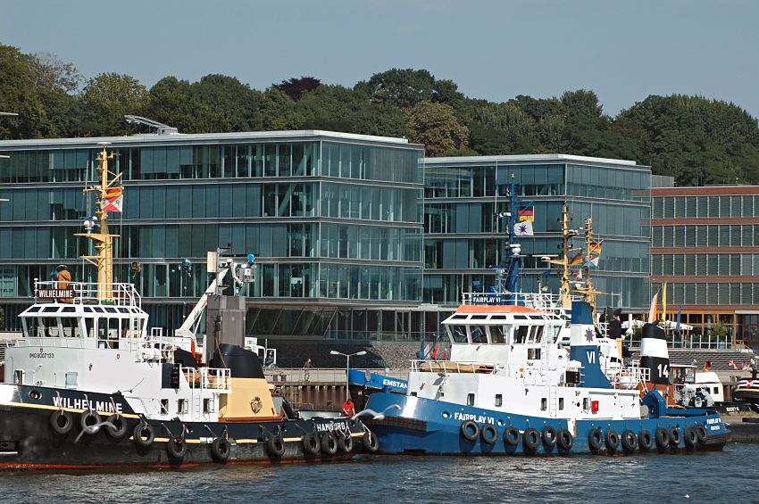 011_26032 |  Die Schlepper WILHELMINE und FAIRPLY VI liegen an Anleger Neumhlen und warten auf grosse Frachtschiffe, die von den PS-starken Arbeitsbooten an ihren Liegeplatz im Hamburger Hafen gebracht werde. Die Schlepper sind mit einer dichten Reihe von Autoreifen bestckt, die das Schiff beim Bugsieren schtzen sollen. Im Hintergrund Hamburgs neue Architektur in Neumhlen am Elbufer - die sogen. architektonische Perlenkette an der  Neumhlen Kaistrasse ist zum Wasser hin hochstehend, damit der untere Bereich der Brogebude vor Hochwasser der Elbe geschtzt sind. Im Hintergrund Bume an der Elbtreppe.  www.christoph-bellin.de 