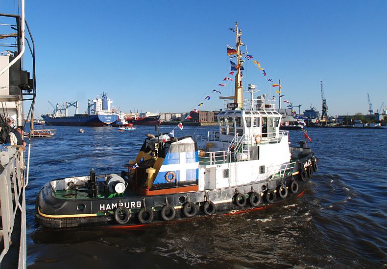 011_26033 |  Bilder aus dem Hafen Hamburgs / Der Schlepper HANS bei einem Einsatz im Hamburger Hafen; das 26m lange Schiff ist mit einem 1740PS starken Motior ausgerstet. Das Heck des Schleppers ist mit einer dicken Gummileiste versehen, mit der das Passagierschiff vorsichtig zum Anlegen an den Kai gedrckt wird. Im Hintergrund das Hafenpanorama von Hamburg - ein grosser Frachter luft ein.   www.christoph-bellin.de 