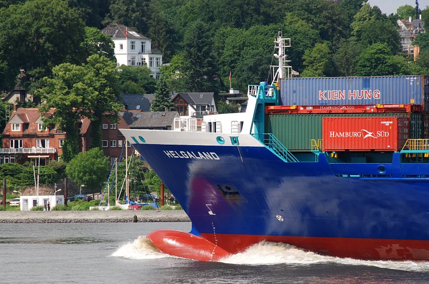 011_26034 |  Das Containerschiff HELGALAND verlsst den Hamburger Hafen - es hat gute Fahrt drauf; am Wulstbug des Container_Feeders ist die weisse Gischt zu sehen. An Deck des Frachters sind Container der unterschiedlichen Reedereien gelagert. Im Hintergrund das grne Hamburg Blankenese mit seinen Husern am Sllberg.  www.christoph-bellin.de