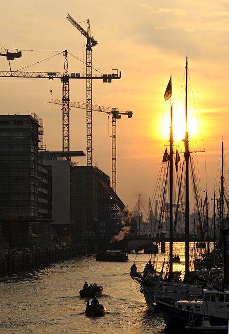 011_26039 |  Sonnenuntergang im Hamburger Hafen - die niedrig stehende Sonne scheint durch die Masten der historischen Segelschiffe im Hamburger Traditionsschiffhafen, der im Sandtorhafen erffnet wurde. Tuckerboote und Festmacher fahren Richtung Elbe, eine Barkasse liegt unter Dampf, der in das Abendrot in den Hamburger Himmel steigt. Lks. die Baustelle in der Hafencity, im Hintergrund Baukrne am Kaispeicher A, wo die Hamburger Elbphilharmonie entstehen soll.   www.christoph-bellin.de 