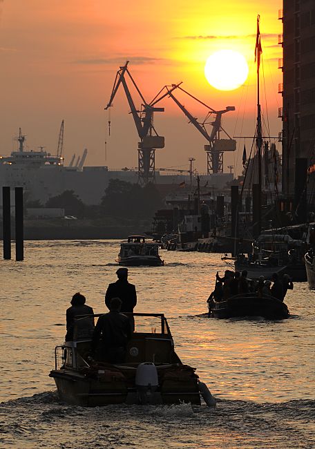 011_26040 |  Sonnenuntergang im Hamburger Hafen - die rote Abendsonne versinkt hinter den Hafenkrnen. Ein Sportboot / Motorboot, ein Festmacherboot und eine Barkasse fahren Richtung Elbe.  www.christoph-bellin.de 