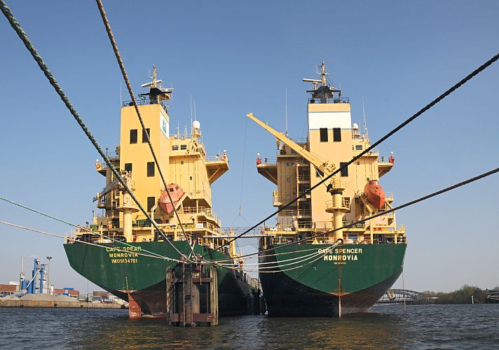 044_85-5872 | Heckansicht aufgelegter Containerfrachter auf der Hamburger Norderelbe, im Hintergrund die Hamburger Elbbrcken. Der Container Transport ist aufgrund der weltweiten Wirtschaftskrise stark zurck gegangen. Aus diesem Grund werden Frachtschiffe stillgelegt; bei einer "heissen" Stilllegung wird das Schiff nur fr eine begrenzte Anzahl von Wochen deaktiviert -  dies geschieht mit einer kleinen Besatzung und kontinuierlicher Maschinenaktivitt. So kann das Schiff in relativ kurzer Zeit wieder in Betrieb genommen werden. Bei einer "kalten" Stilllegung wird das Schiff fr lngere Zeit "vom Markt" genommen, eine Reaktivierung ist dann recht langwierig und kann bis zu drei Monaten dauern. www.fotograf-hamburg.de