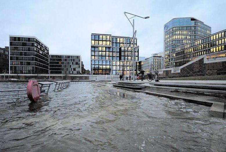 7890_0955 Eine Sturmflut hat Teile der Marco-Polo-Terrassen in dem Hamburger Stadtteil Hafencity unter Wasser gesetzt - ein Rettungsring am Gelnder der Terrassen wird vom Wasser umsplt. Die Kaimauern des Grasbrookhafens sind nicht mehr zu erkennen. Passanten stehen an den Terrassen und beobachten das Geschehen - im Hintergrund Brohuser mit erleuchteten Fenstern. Hochwasser in der Hamburger Hafencity - Marco Polo Terrassen unter Wasser. 