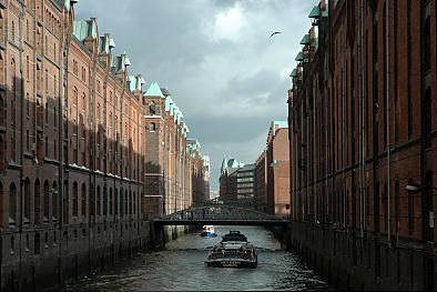 011_25845 | Blick auf einen Fleet in der Hamburger Speicherstadt; Schiffe fahren auf dem Kanal - auf beiden Seiten die Lagerhuser des ehem. Freihafens, die Sonne scheint auf die Kupferdach-Giebel der Backsteingebude.